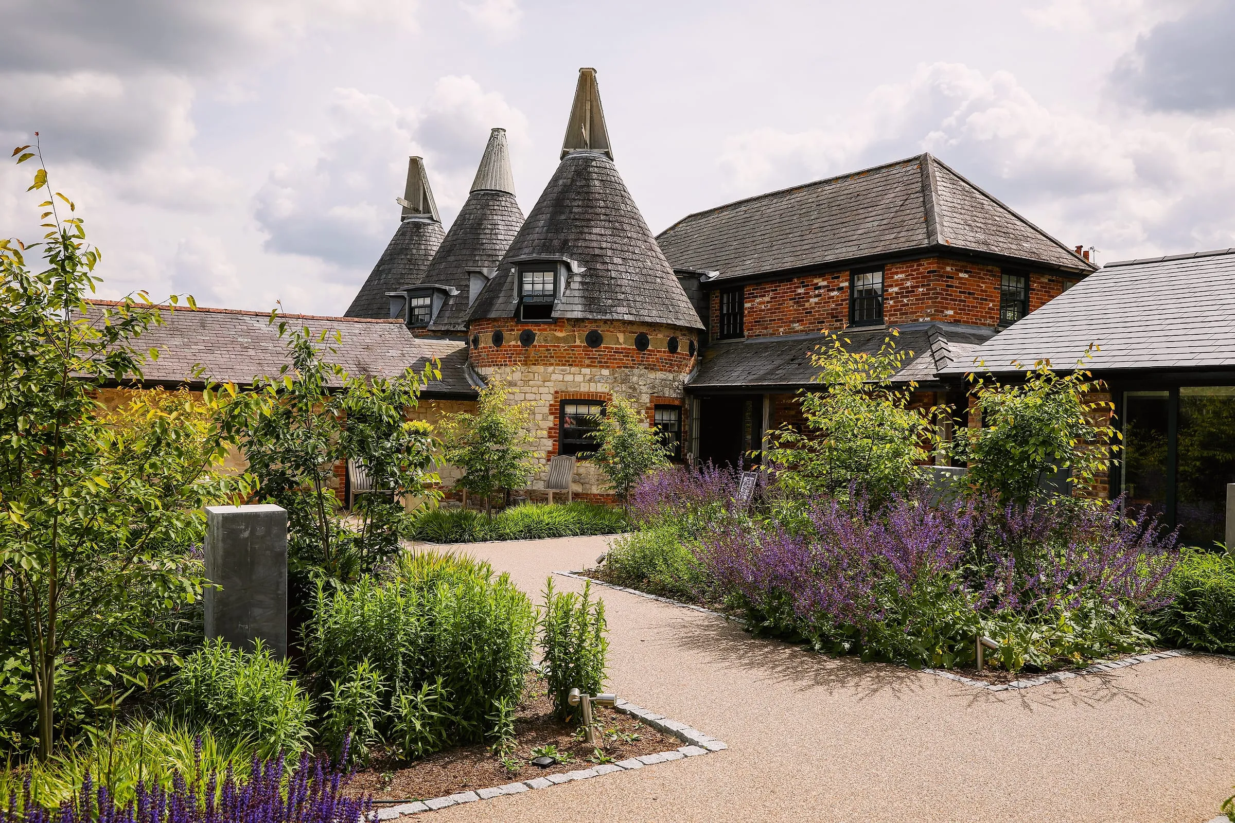 Three oast roundels above the entrance courtyard, with salvia and young trees along the drive